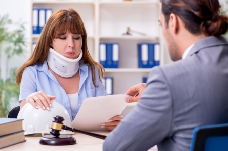 Woman wearing a neck brace reviewing documents with a personal injury attorney in an office.